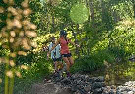 Zwei Frauen wandern über einen Bach im Wald bei Pontresina in den Engadiner Alpen