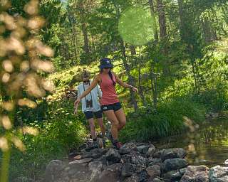 Zwei Frauen wandern über einen Bach im Wald bei Pontresina in den Engadiner Alpen