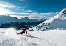 Skifahrer in roter Jacke zieht elegante Kurven auf frisch präparierter Piste in Corviglia, Engadiner Berge im Hintergrund