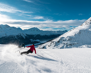 Skifahrer in roter Jacke carvt über die Piste in Corviglia bei St. Moritz, im Hintergrund Engadiner Bergpanorama
