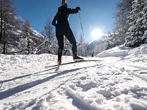 Langläuferin auf verschneiter Loipe in Pontresina mit schneebedeckten Lärchen und strahlender Wintersonne