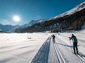 Zwei Langläufer auf einer präparierten Loipe in Pontresina bei strahlendem Sonnenschein und Bergpanorama.