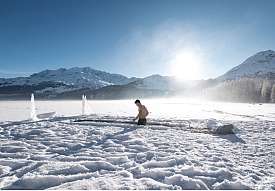 Mann beim winterlichen Eisbaden im zugefrorenen See vor Engadiner Bergpanorama