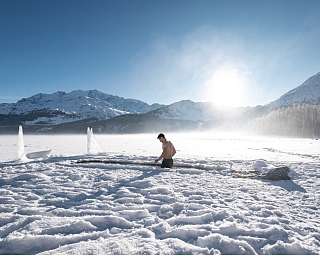 Mann beim Eisbaden im zugefrorenen Silsersee bei Pontresina, umgeben von schneebedeckten Bergen im Engadin