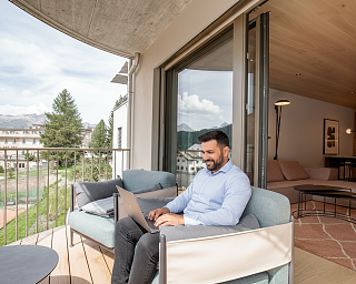 Man working on a laptop on the balcony of a room at Sunstar Hotel Pontresina with views of the Engadine mountains and landscape.